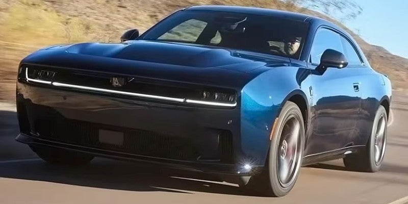 A navy blue modern muscle car with a glowing rectangular light bar across the front, driving on a road