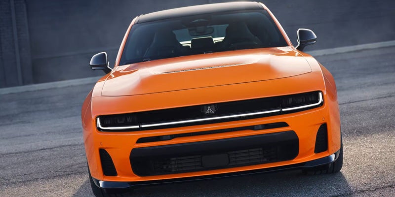 Front view of a shiny orange Dodge Charger, a black roof and grill, and modern LED headlights