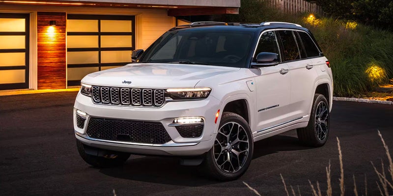 White Jeep Grand Cherokee L 4xe parked in front of a modern garage with illuminated translucent doors
