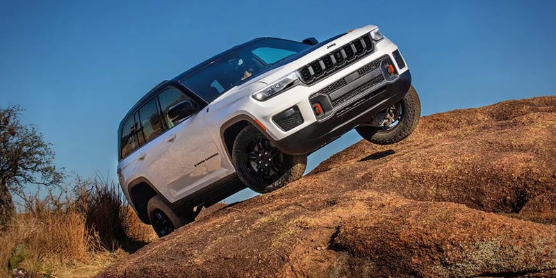 A white Jeep Grand Cherokee, with black trim and wheels, off-roading up a steep, rocky, reddish-brown incline