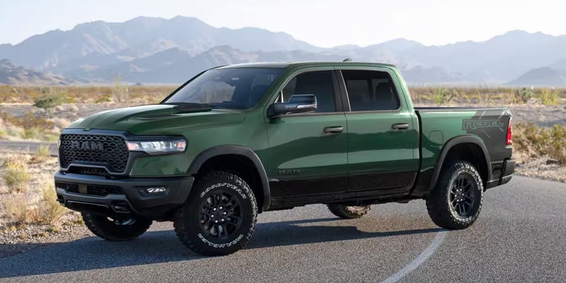 A green Ram Rebel pickup truck with black trim and wheels on a road in a desert landscape