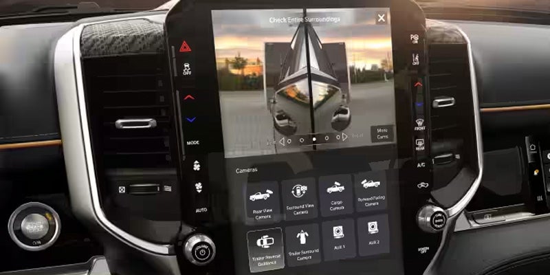 A car's dashboard screen displays multiple camera views, including a trailer with a boat and backup camera options