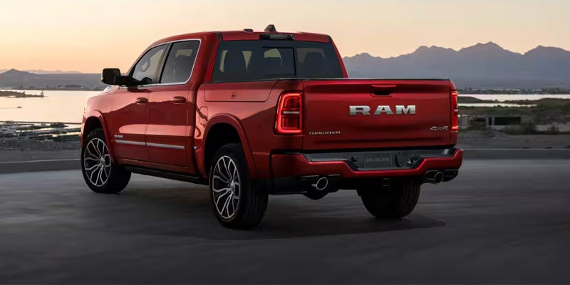 Shiny red Ram pickup truck parked on asphalt with a body of water and mountains in the background at sunset