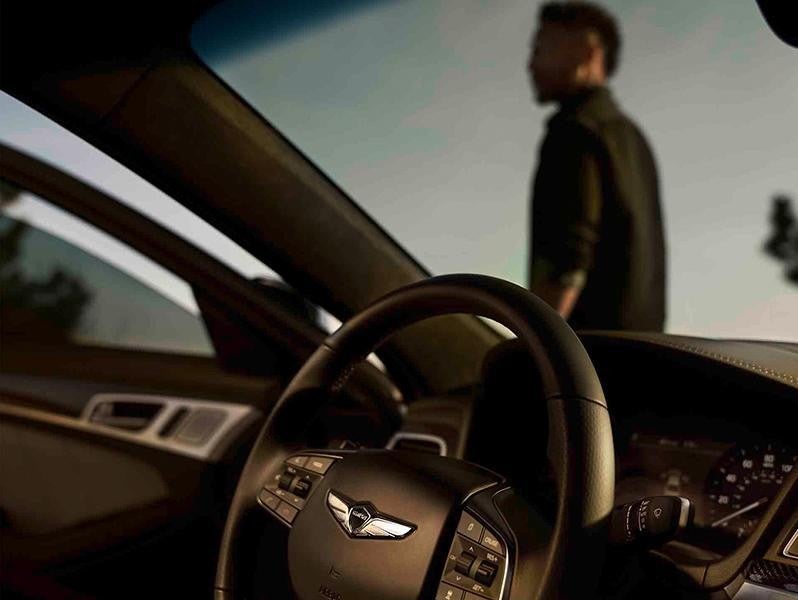 Interior view of a car with a black steering wheel, dashboard, and open door. A man stands outside