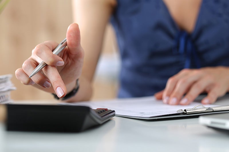 A person's hands operating a calculator and writing on a document