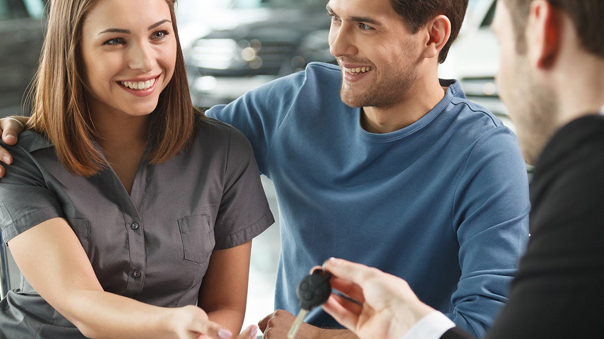 Happy couple receiving car keys from a salesperson after finalizing a purchase