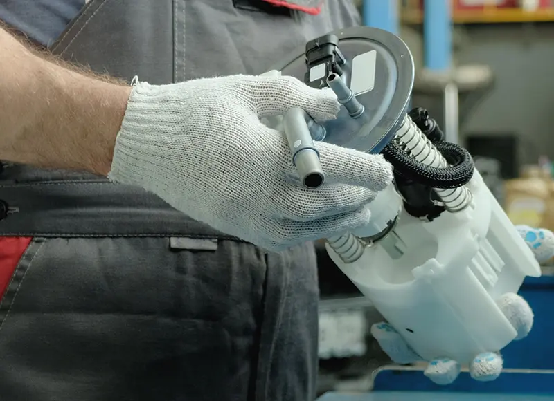 Close-up of a mechanic in white gloves holding a fuel pump with a gray top and white plastic base