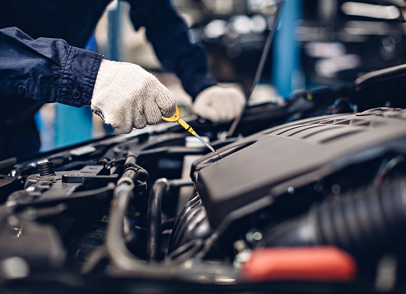 Gloved hand checking the oil with a yellow dipstick in a car engine compartment