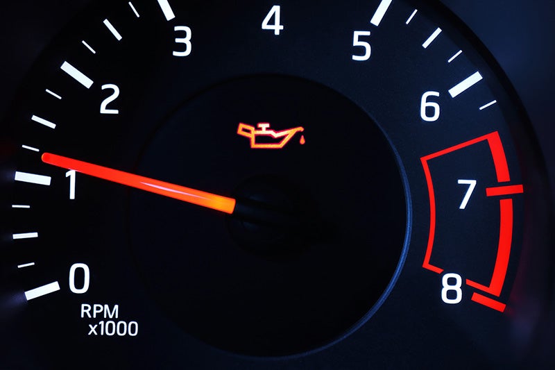 Close-up of a vehicle dashboard tachometer with the engine oil warning light illuminated in the center