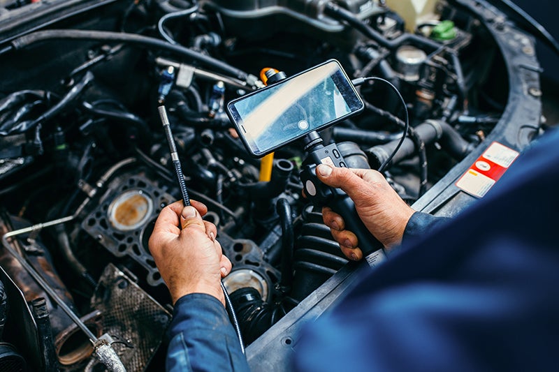 Mechanic uses a borescope attached to a smartphone to inspect a car engine from above